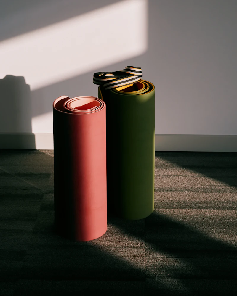 Zwei aufgerollte Yogamatten lehnen im Abendlicht an einer hellen Wand.