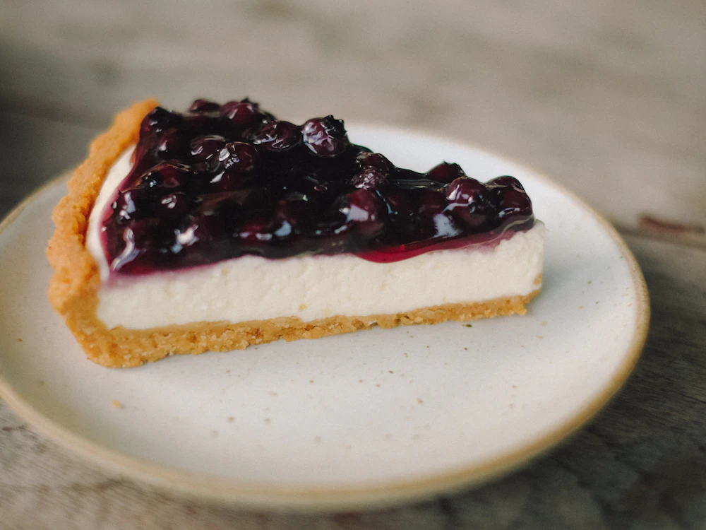 Ein Stück Käsekuchen mit Blaubeeren auf einem hellen Teller