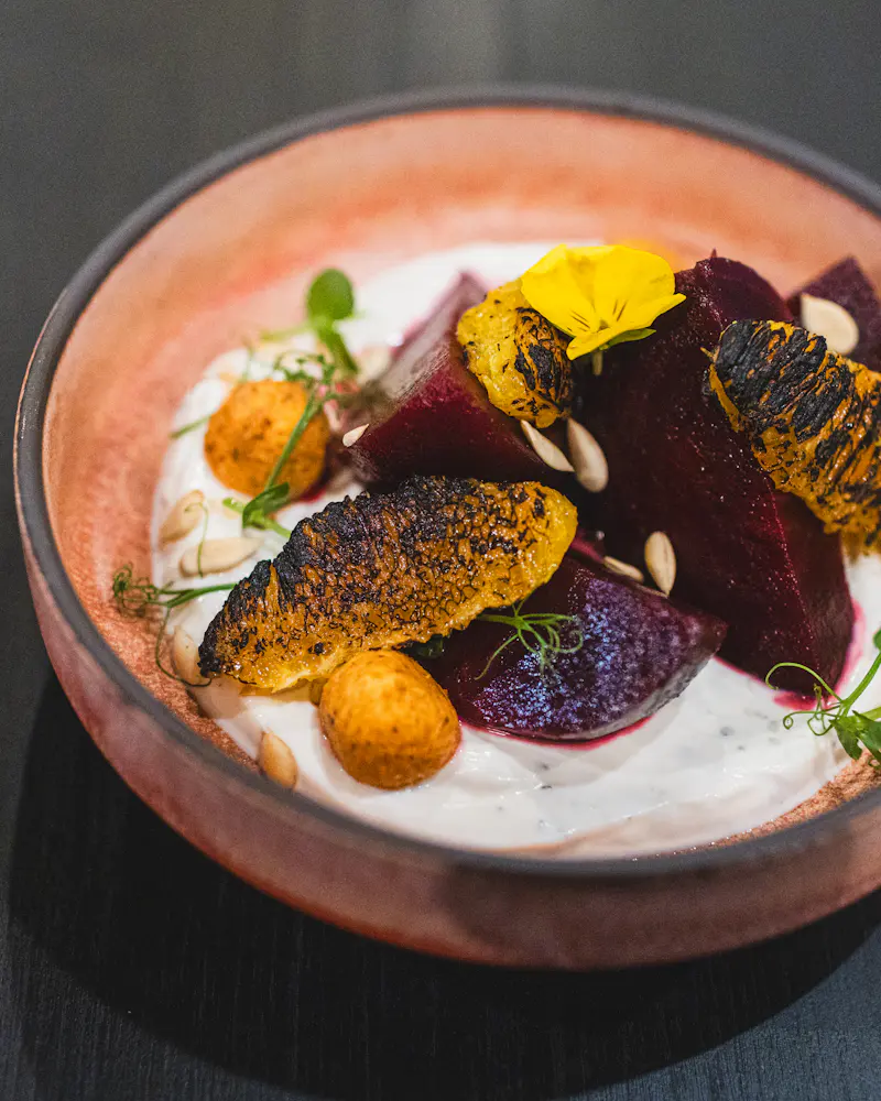 Rote Bete mit Joghurt, gerösteten Kernen und einer essbaren Blüte in einer rosa Keramikschale